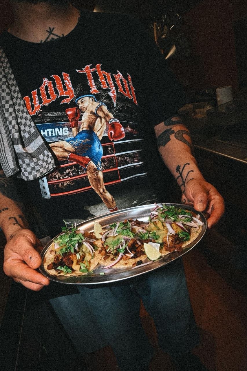 Plato grande con varios tacos, salsas, lima y rábano, sobre superficie oscura.